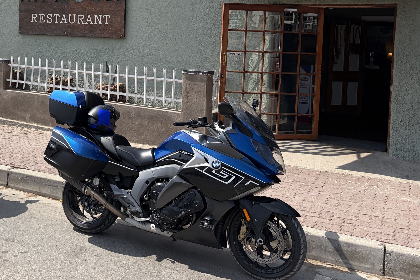 A blue BMW K1600 GT parked on a quiet Great Karoo street outside a small restaurant.