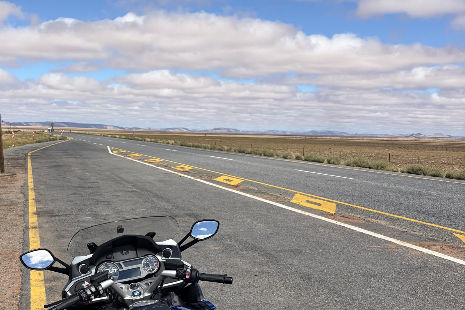 A BMW K1600 GT parked on a quiet open road, with big sky and flat plains stretching to the horizon.